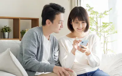 撮影の最初のステップである予約を表す写真で、男女カップルが自宅でくつろぎながらスマホからスタジオグッドの撮影予約を行っています。